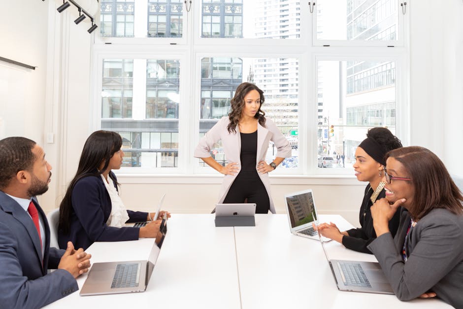 A diverse group of professionals engaged in a meeting at a modern office with laptops and city view.
